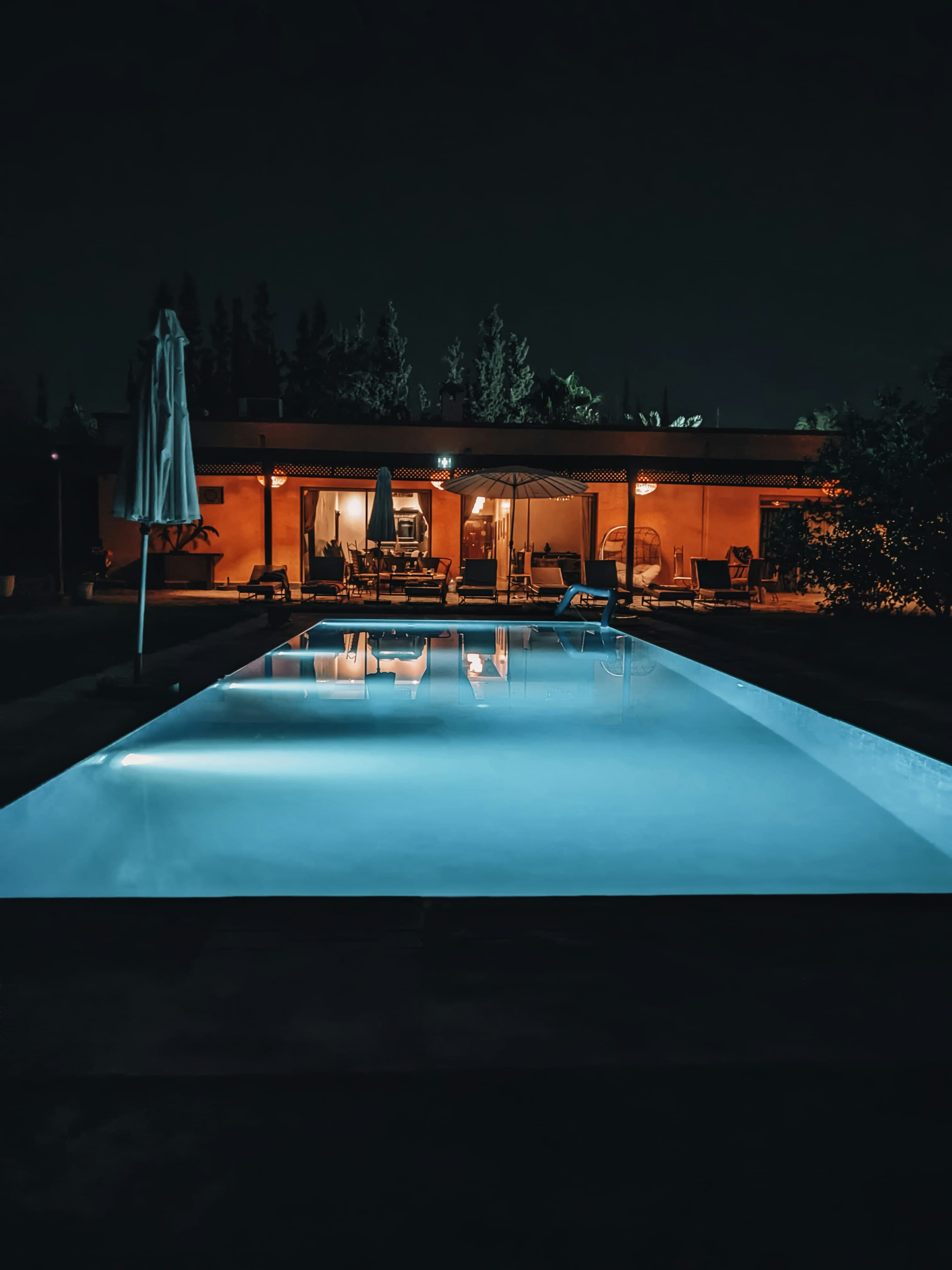 A suburban backyard pool lit from below at night, the house dark behind it