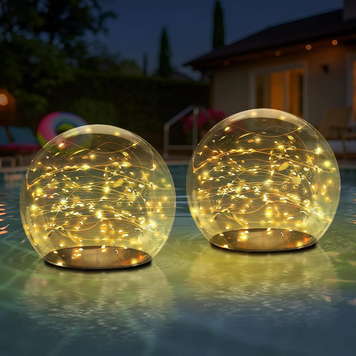 Two glass globes lit with warm wire lights, floating on a pool at dusk