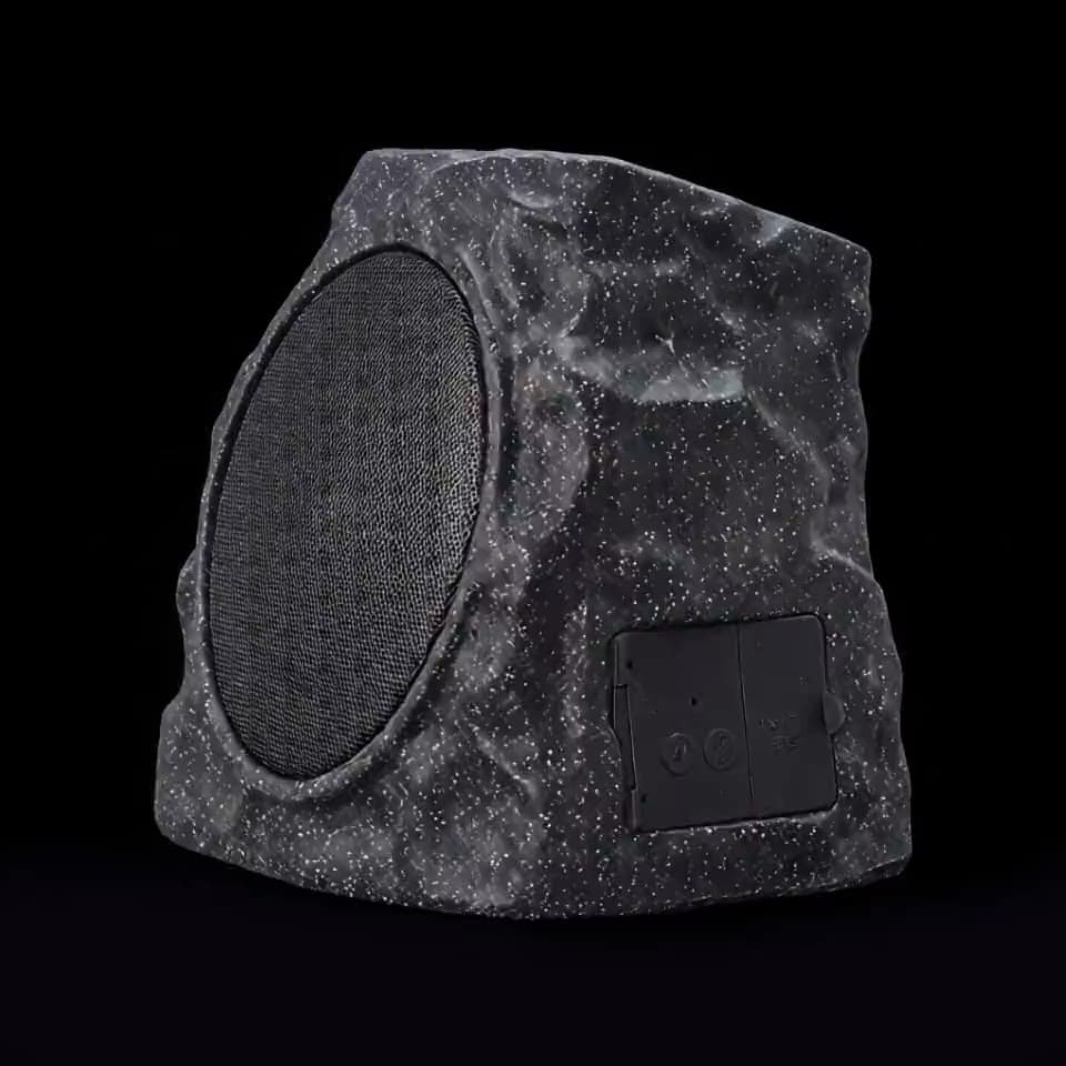 A rock-shaped outdoor speaker turning slowly against black, its speaker grille coming into view