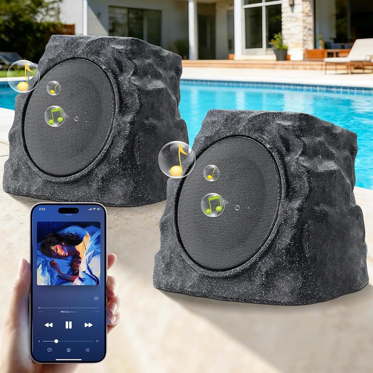 Two rock-shaped speakers on a poolside deck, a phone controlling them alongside